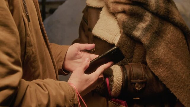 Cropped shot of unrecognizable couple using ride-sharing mobile application on smartphone outdoors in winter. Perfect for commercial advertisements of on-demand delivery and transport services