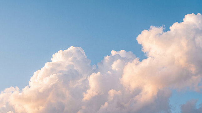 Majestic and fluffy cumulus clouds dramatically lit by the warm, golden glow of the sun against a clear blue sky.