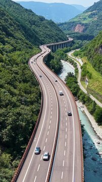 Vertical drone view of the Autostrada del Brennero crossing a scenic alpine valley alongside a mountain river in northern Italy