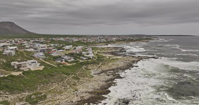 Gansbaai South Africa Aerial v3 flyover around De Kelders and Stanford's Cove homes along a rocky coast beneath mountains and overcast skies - Shot with Mavic 3 Pro Cine - Jan 7th 2024