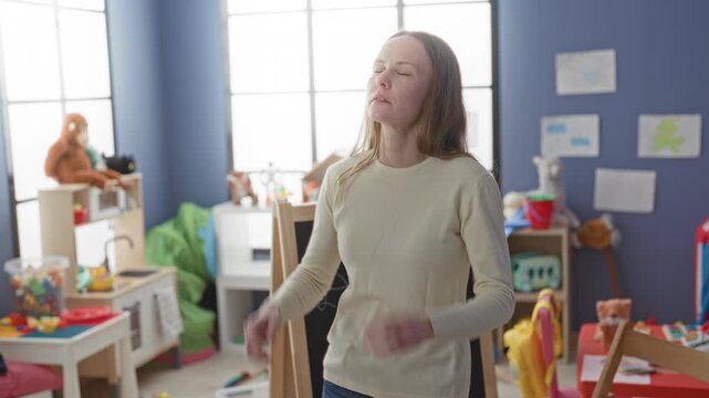 Woman pressing temples in a cluttered preschool playroom building with toys, chalkboard and tent visible; stress overwhelm fatigue.