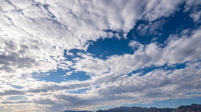 Majestic blue sky filled with swirling white and gray cumulus clouds, towering over a distant mountain range.