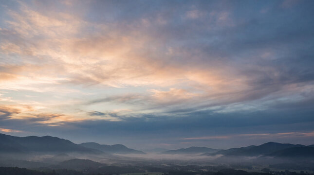 Dramatic mountain landscape view at dawn or dusk with misty valleys below and a vibrant, colorful sky above.