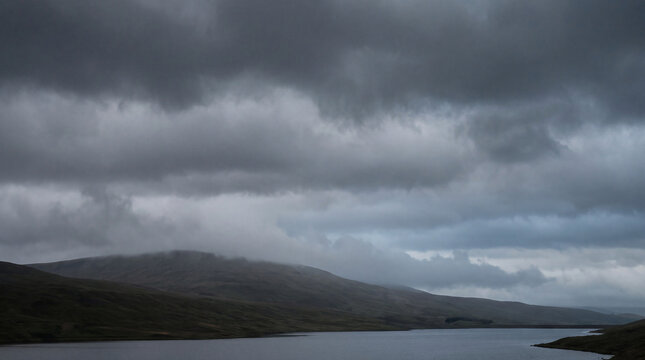Gloomy, low-lying mist and dark clouds hover over a tranquil lake and somber rolling hills.