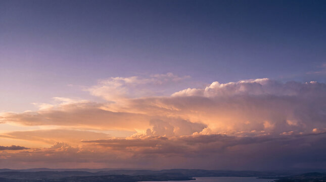 Dramatic sunset clouds glow with golden light above a serene lake and distant mountains under a vast, colorful sky.