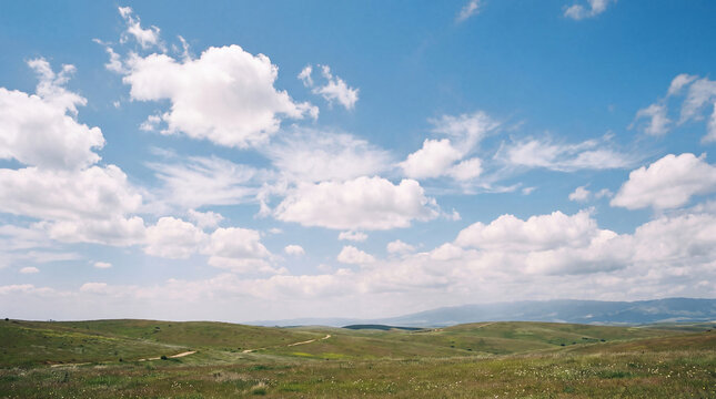 Expansive green rolling hills under a vibrant blue sky with fluffy white clouds, peaceful natural landscape.
