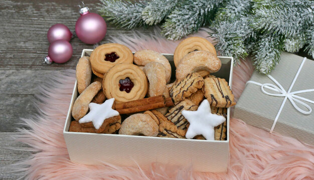 Eine Auswahl an traditionellen Weihnachtspl&auml;tzchen in einer Geschenkbox . Zimtsterne, Vanillekipferl und Linzer Kekse auf rosa Kunstfell mit Weihnachtsdeko.