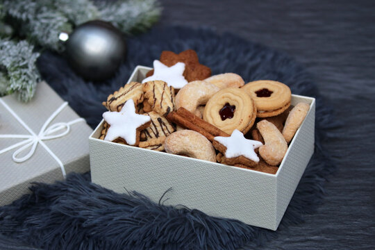 A selection of traditional Christmas cookies in a gift box. Cinnamon stars, vanilla crescents, and Linzer cookies on faux fur with Christmas decorations.
