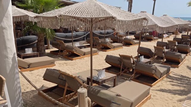Multiple rows of sun loungers stretch across a sandy beach resort shaded by large white umbrellas
