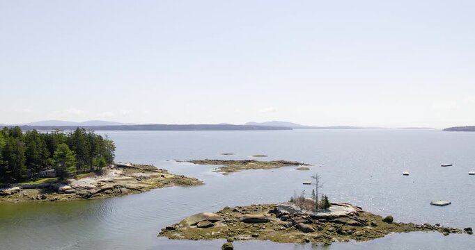 A sweeping aerial shows the quiet Maine coast with islands trees and open water in clear daylight