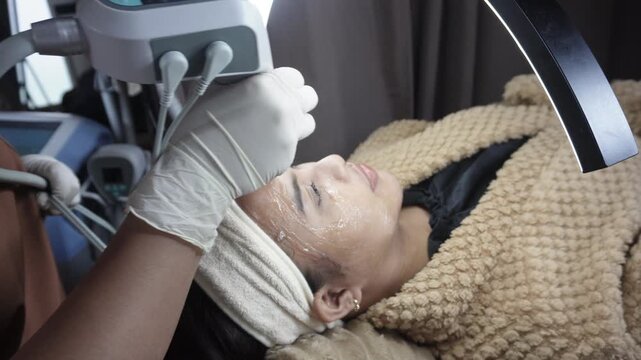 Female patient receiving dual radiofrequency and ultrasound facial treatment on the cheeks at an aesthetic clinic for skin tightening. Currently on forehead.
