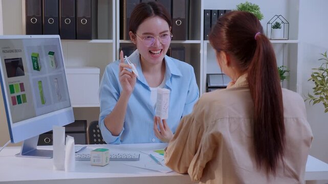 Two asian woman graphic designer using artificial intelligence designing cosmetic packaging box in office, looking at prototype mockup on computer screen, creative agency developing cosmetic product.