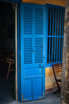 Vintage blue colored wooden doors and table with chairs setting in traditional cafe in Hoi An, Vietnam, authentic exterior of Vietnamese cafe with old wooden doors and window shutters in ancient style