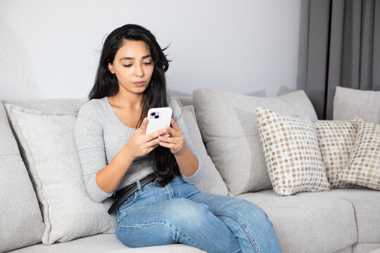 woman is using a phone sitting on a sofa