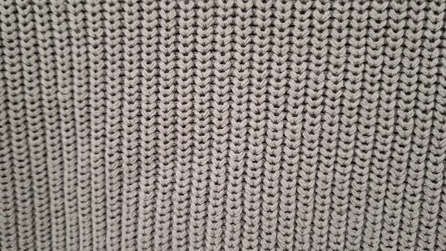 Close-up texture of grey knitted fabric wool clothes, warm winter wardrobe background, fashion textile detail. gray geometric textile pattern with woven surface,  decorative texture.