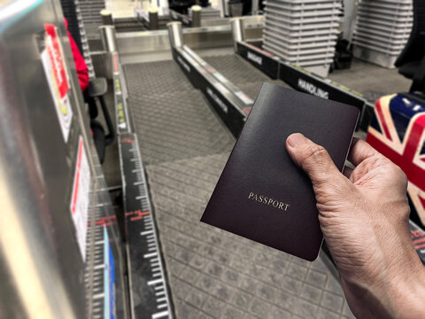 passport in right hand while standing near airport baggage weight scale conveyor travel document and luggage check-in equipment represent international travel, departure, tourism, journey, and custom
