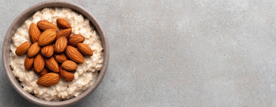 Bowl of oatmeal topped with whole almonds on rustic stone surface with copy space for healthy breakfast and clean eating nutrition lifestyle concepts
