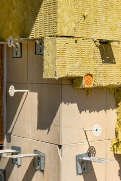 Workers are using insulation and tiles for a construction project at a building site. Tools and materials are visible on the exterior of the structure