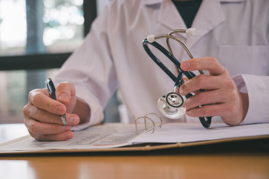 Male doctor wearing white cloth and stethoscope using pen and paper report analysing patient diagnosis data in medicine and healthcare concept