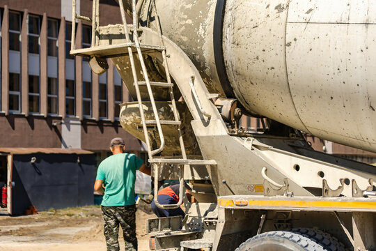 A concrete mixer truck stands at a construction site. Workers are preparing concrete for use in ongoing building work. Several materials are scattered around.