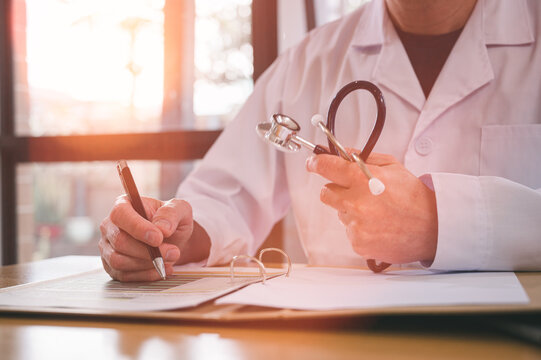 Male doctor wearing white cloth and stethoscope using pen and paper report analysing patient diagnosis data in medicine and healthcare concept