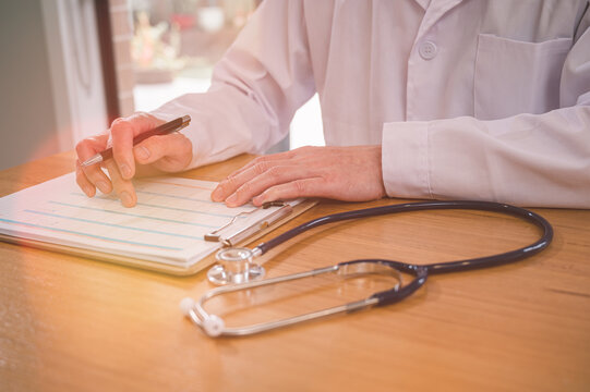 Male doctor wearing white cloth and stethoscope using pen and paper report analysing patient diagnosis data in medicine and healthcare concept