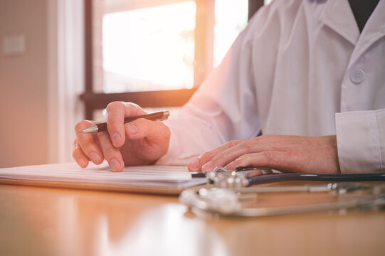 Male doctor wearing white cloth and stethoscope using pen and paper report analysing patient diagnosis data in medicine and healthcare concept
