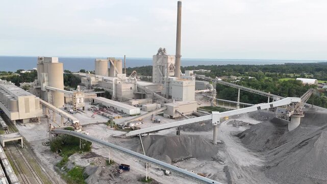 High-angle stationary shot looking down at the industrial conveyor bridge networks, production buildings, kiln smokestack, and grey gravel aggregate piles of the Ash Grove Cement Plant in Mississauga