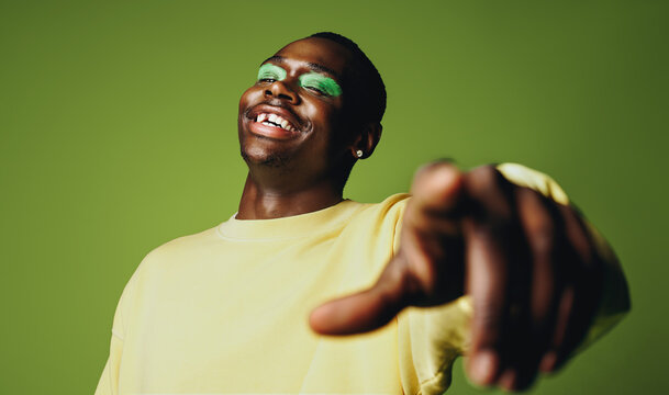 Man pointing in the studio with laughter, camera focus, and bold makeup