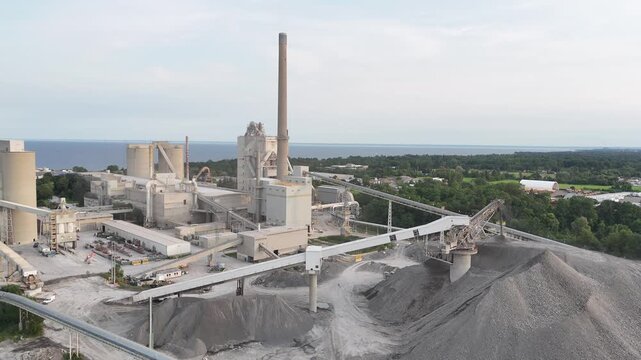 High-angle stationary shot looking down at the industrial conveyor belts, kiln smokestack, and aggregate stone piles of the Ash Grove Cement Plant on Lake Ontario in Mississauga, Canada