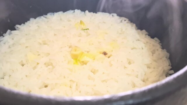 Close up shot of freshly cooked, steaming white rice with garlic bits in a traditional black pot. Hot, fluffy, and delicious Asian cuisine.