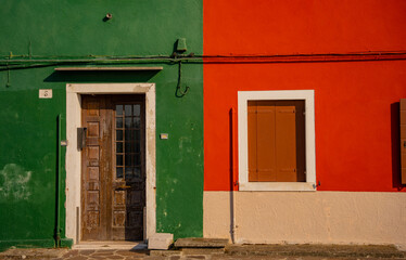 Fototapeta premium Colorful green and orange facade of a traditional house with wooden door and shuttered window in Burano island, Venice, Italy