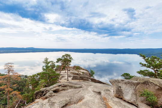 Green pine tree grows among stones on peak of mount Bolektay and panoramic view on Burabay Borovoe Lake, blue cloud sky. Burabay National Nature Park in Republic Kazakhstan. Summer scenery landscape.