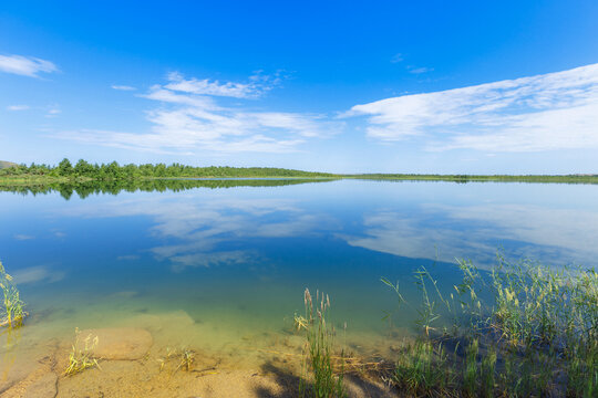 Stony shore lake Ulken Shabakty with blue water and reflection of green plants and blue sky with white clouds. Beautiful scenic landscape in Burabay National Nature Park. Summer nature travel photo.