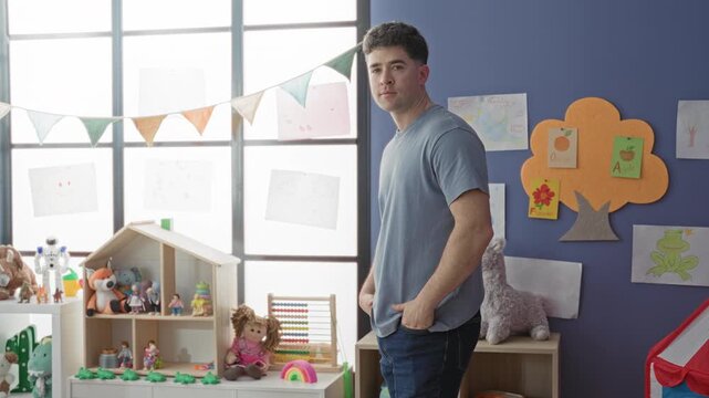 Man standing with hands in pockets beside toy shelf and dollhouse in a preschool classroom building, smiling toward camera; warmth.