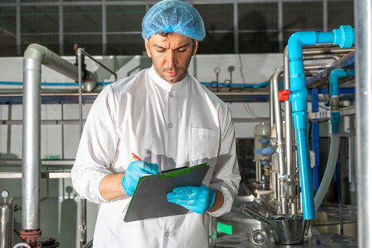 Confident mature male worker in white uniform and blue rubber gloves working in food factory.