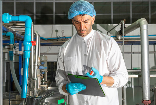 Confident mature male worker in white uniform and blue rubber gloves working in food factory.