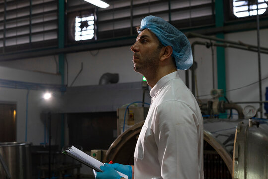 Confident mature male worker in white uniform and blue rubber gloves working in food factory.