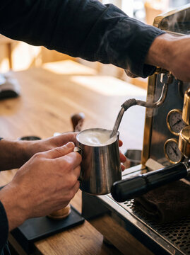 Close-up of barista hands steaming milk with steam wand on espresso machine in warm cafe light