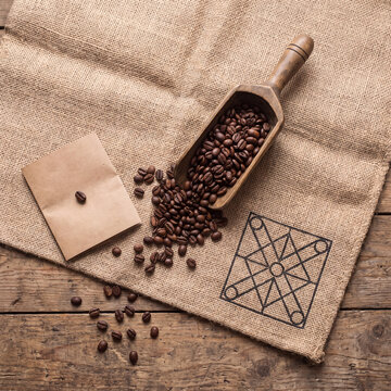 Overhead flat lay of burlap coffee sack with wooden scoop of roasted beans and craft paper on wood floor
