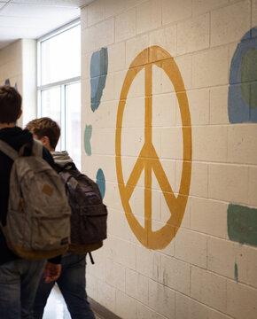 Large yellow peace sign painted on school hallway wall with blurred students walking past in bright light