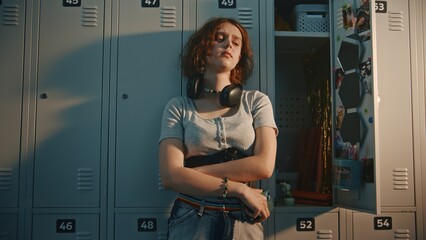 Teenage Schoolgirl With Headphones at Neck Standing in High School Locker Room. Girl Holds...