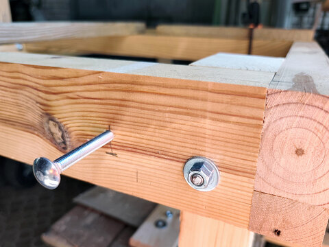 Carriage bolt fastening a wooden frame during assembly. Close-up of timber construction with metal hardware for woodworking, carpentry, DIY furniture building and home improvement.
