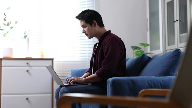 Young asian man working from home on a laptop and getting progressively more tired.