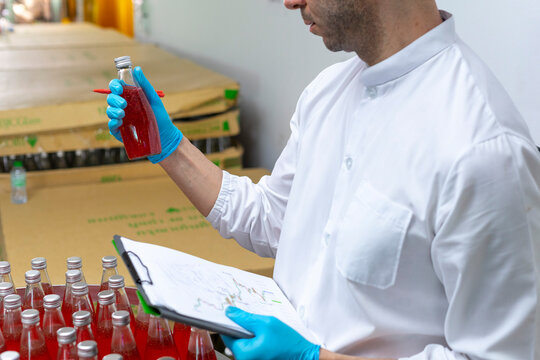 Portrait of mature male researcher with bottle of red beverage in bottle factory.