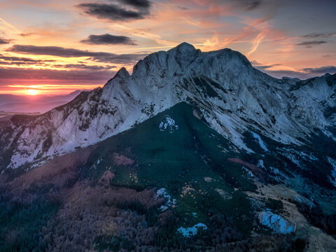 Aerial view of the rugged peaks of Sutjeska National Park at sunset, with rocky slopes, dense pine forests, and a vibrant orange sky in Tjentiste, Republika Srpska, Bosnia and Herzegovina.