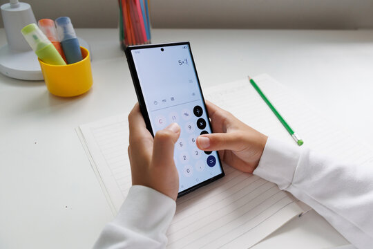 Child calculating a math problem with a smartphone calculator during homework. Mobile technology provides a practical digital tool for mathematics, calculations and home learning.