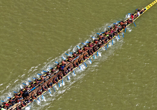 Aerial view of a traditional long boat with numerous rowers paddling in unison across the river in Sirajganj, Rajshahi Division, Bangladesh.