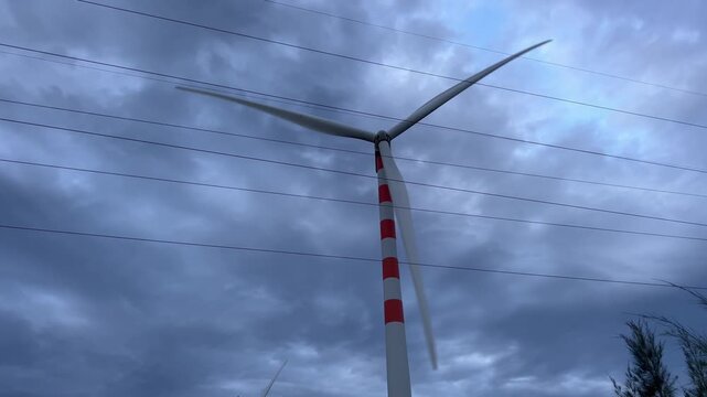 Handheld shot of large wind turbine spinning at twilight against dramatic stormy sky with power lines in Quy Nhon Vietnam