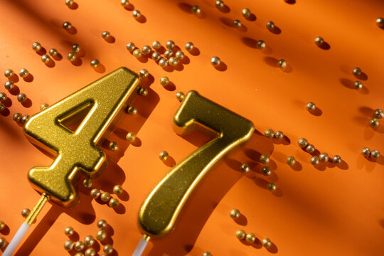 vibrant festive backdrop for 47th birthday, made of gold candles shaped like number forty-seven, placed on an orange background with sprinkles. versatile festive banner